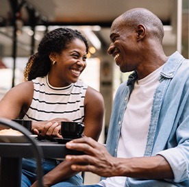 Couple smiling while enjoying cup of coffee outside