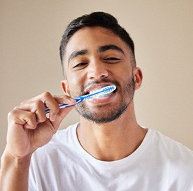 Smiling patient in white shirt brushing their teeth
