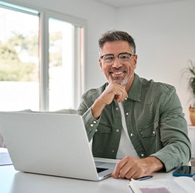 Man with glasses smiling while working on laptop