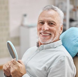 a patient smiling while checking his teeth with a mirror