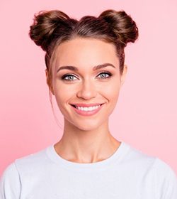 young woman with hair in space buns smiling against pink background 