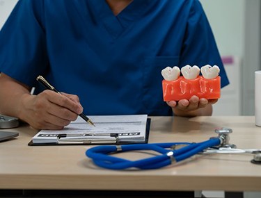 Dentist holding a model of three consecutive teeth while filling out a form