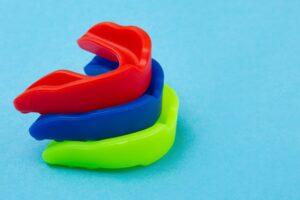 Red, blue, and green mouthguards stacked on a light blue background