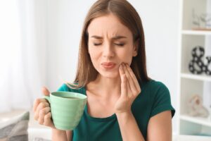 Woman suffering from sensitive tooth while holding coffee cup.